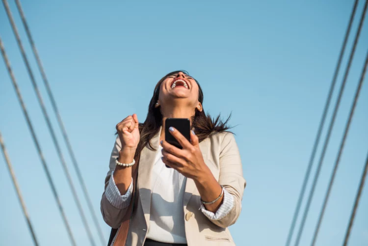 Woman laughing to the sky in happiness holding phone outdoor.