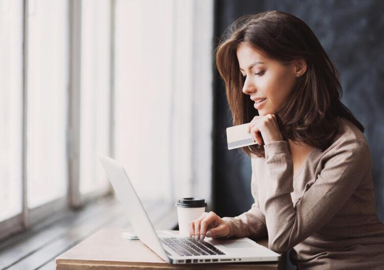 Young woman holding credit card and using laptop computer.