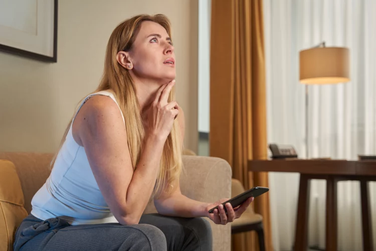 Woman looking up and thinking while holding smartphone