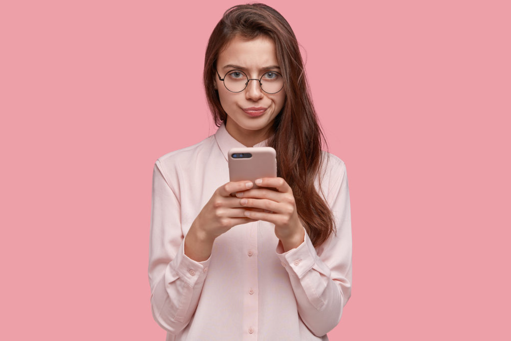 Girl with a displeased expression holding her cellphone with a pink background.