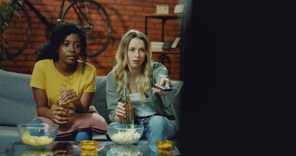 Girls having popcorn and drinks in front of the television.