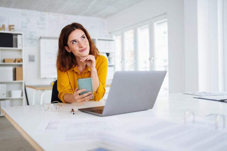 young modern woman holds her cell phone in the office and looks up thoughtfully