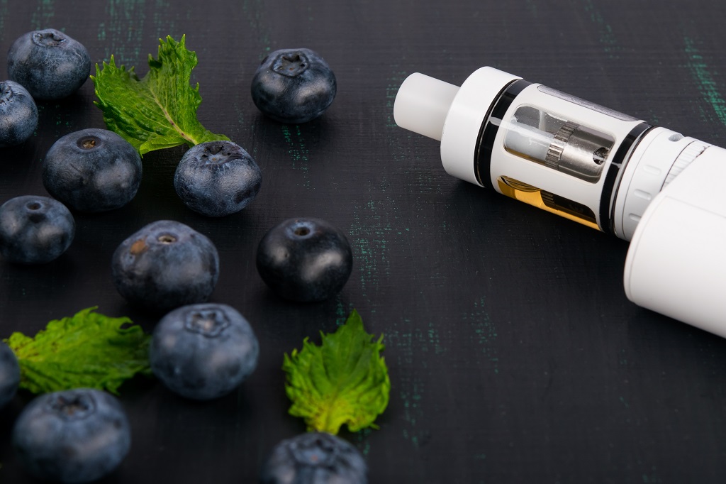 White electronic cigarette on a dark table, next to a scattered berries.