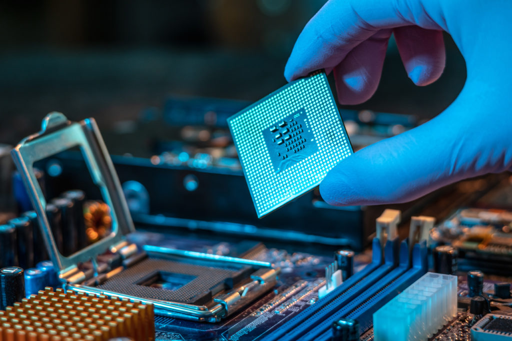 Engineer's gloved hand holding the CPU chip with motherboard on the background.