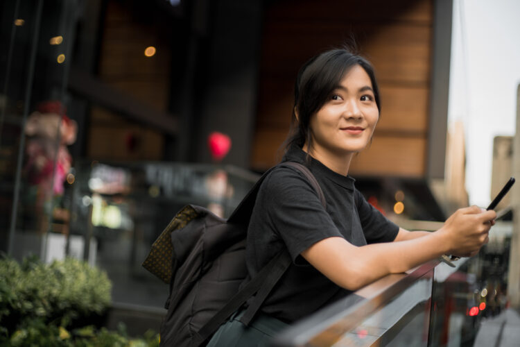 Happy asian woman looking at her phone in the city