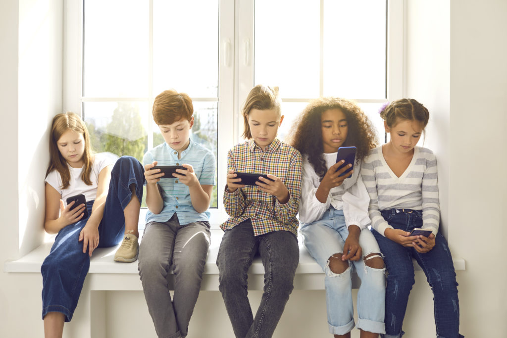 Children sitting on windowsill, playing with their mobile phones.