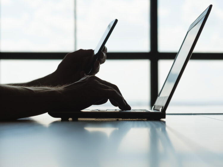 male hand typing on laptop and holding smartphone