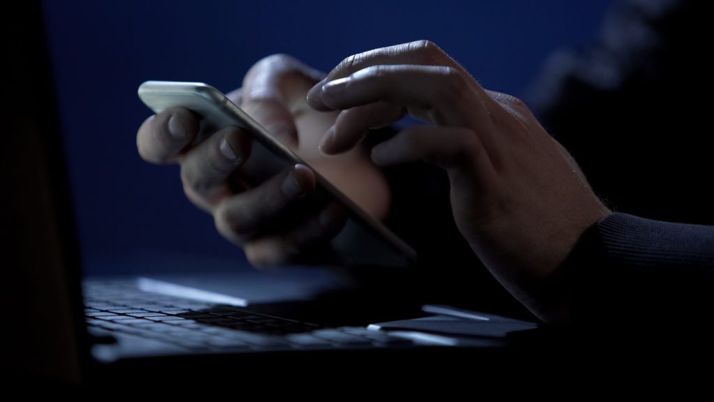 Hacker using smartphone inside a dark room.