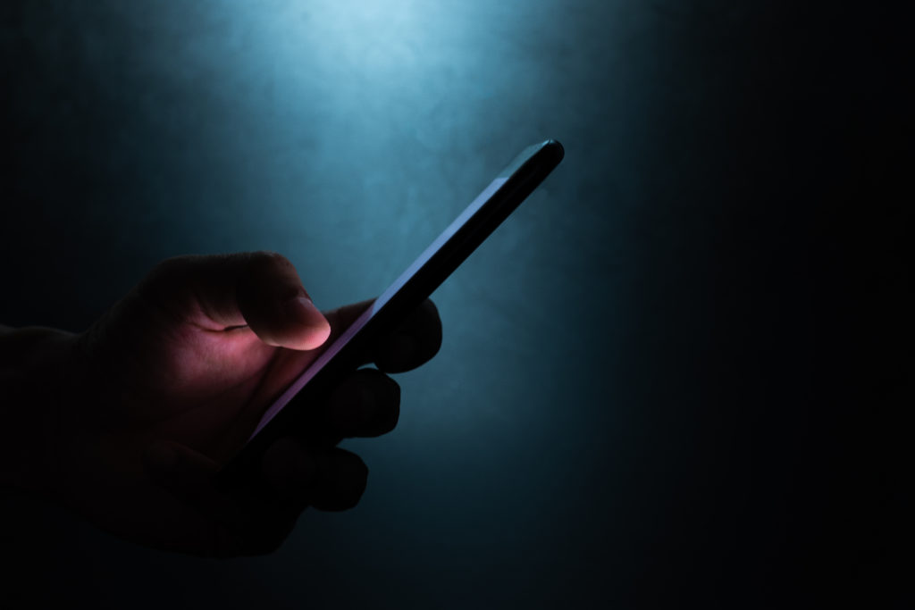 silhouette of hand holding and touching a mobile phone screen in the dark.