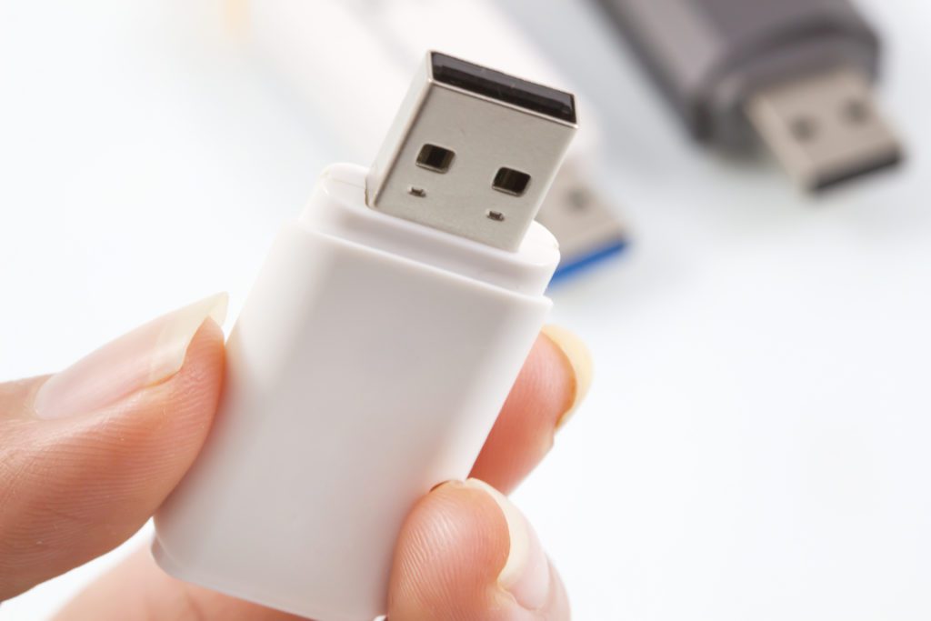 Hand holding white USB drive on white background.