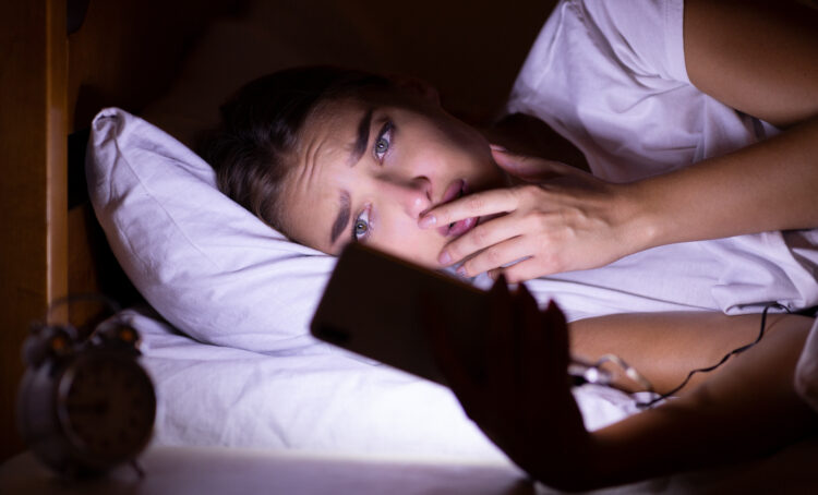 Anxious girl using cellphone lying in bed at night