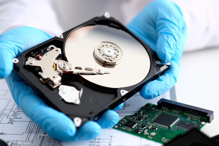A male repairman wearing blue gloves holding hard disk drive