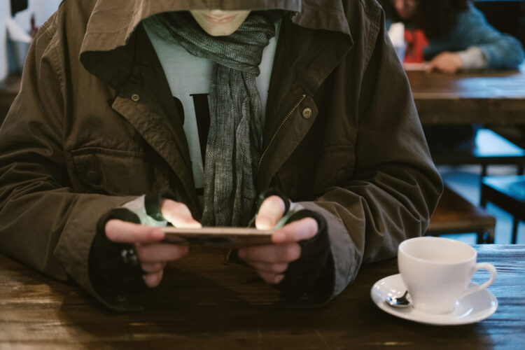 Young male wearing hoody using cell phone seating in cafe with cup of tea