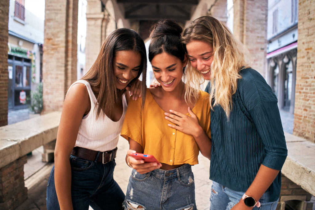 Three happy women watching social media content on smartphone.