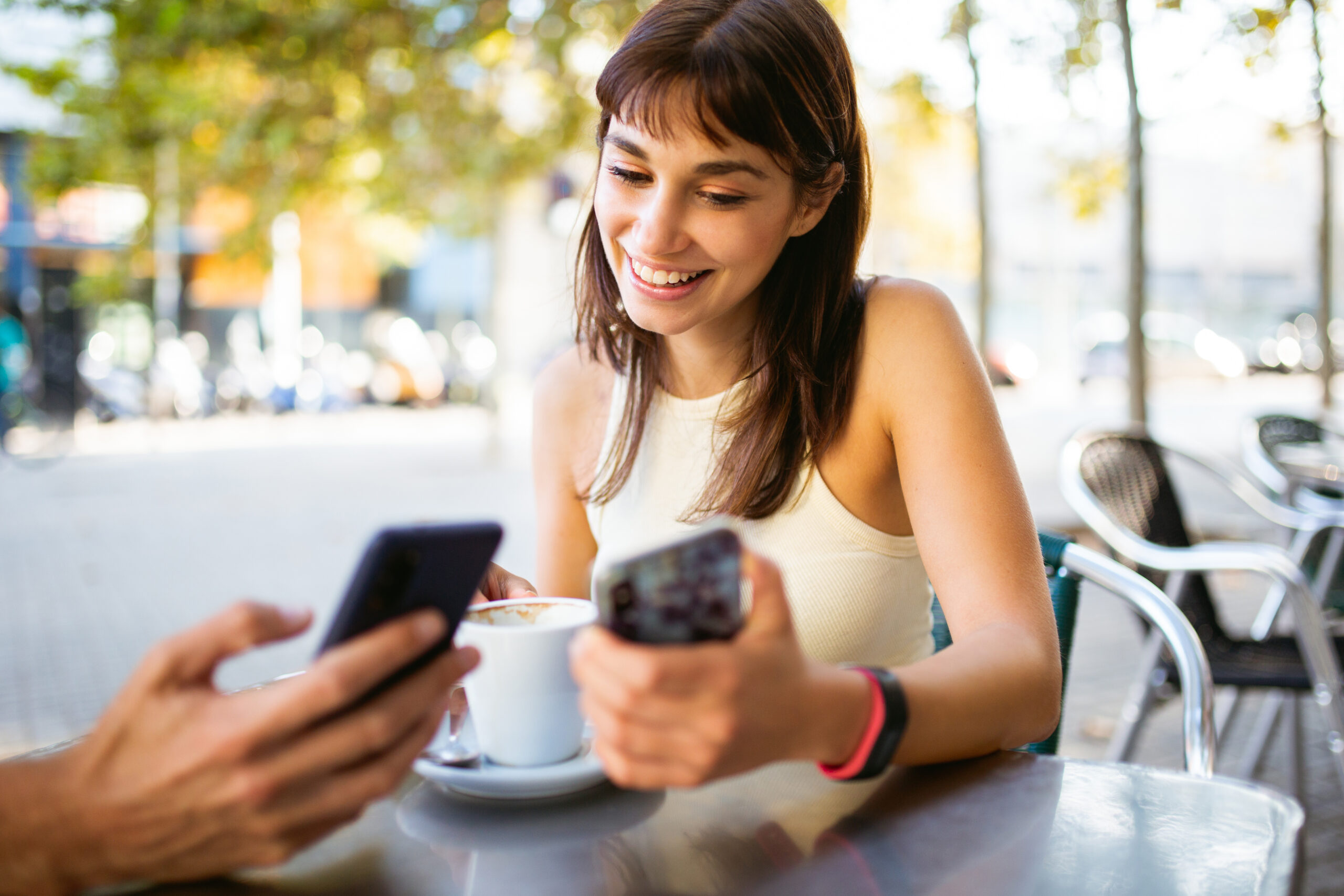 Smiling young woman using phone with friend at outdoor cafe