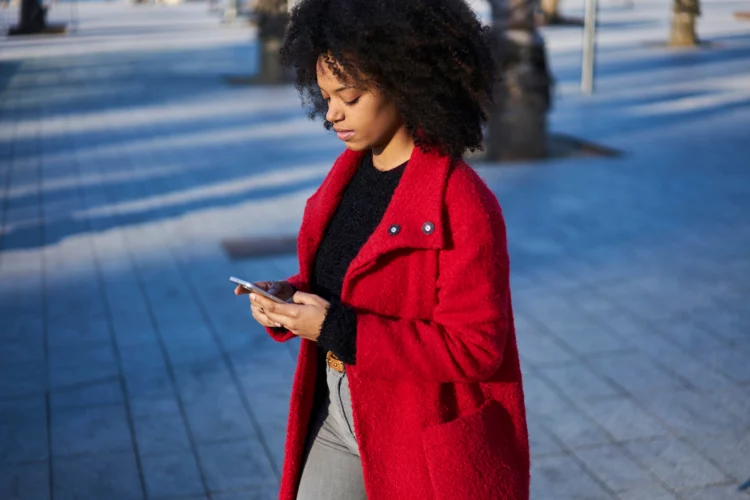 Confident afro woman in red coat messaging on smartphone