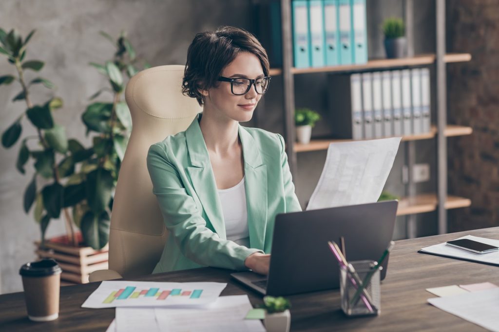 Attractive woman with glasses working on laptop at workplace.