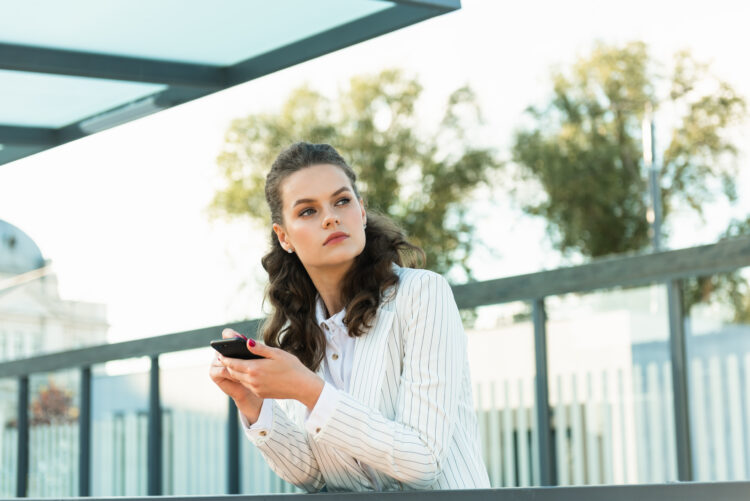 Serious young woman checking cell phone outdoors. 