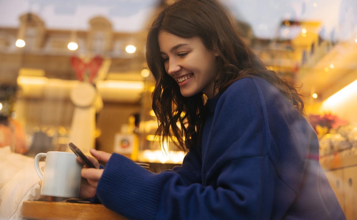 Smiling young girl sits in cafe on phone wondering does Instagram invert your face on calls?