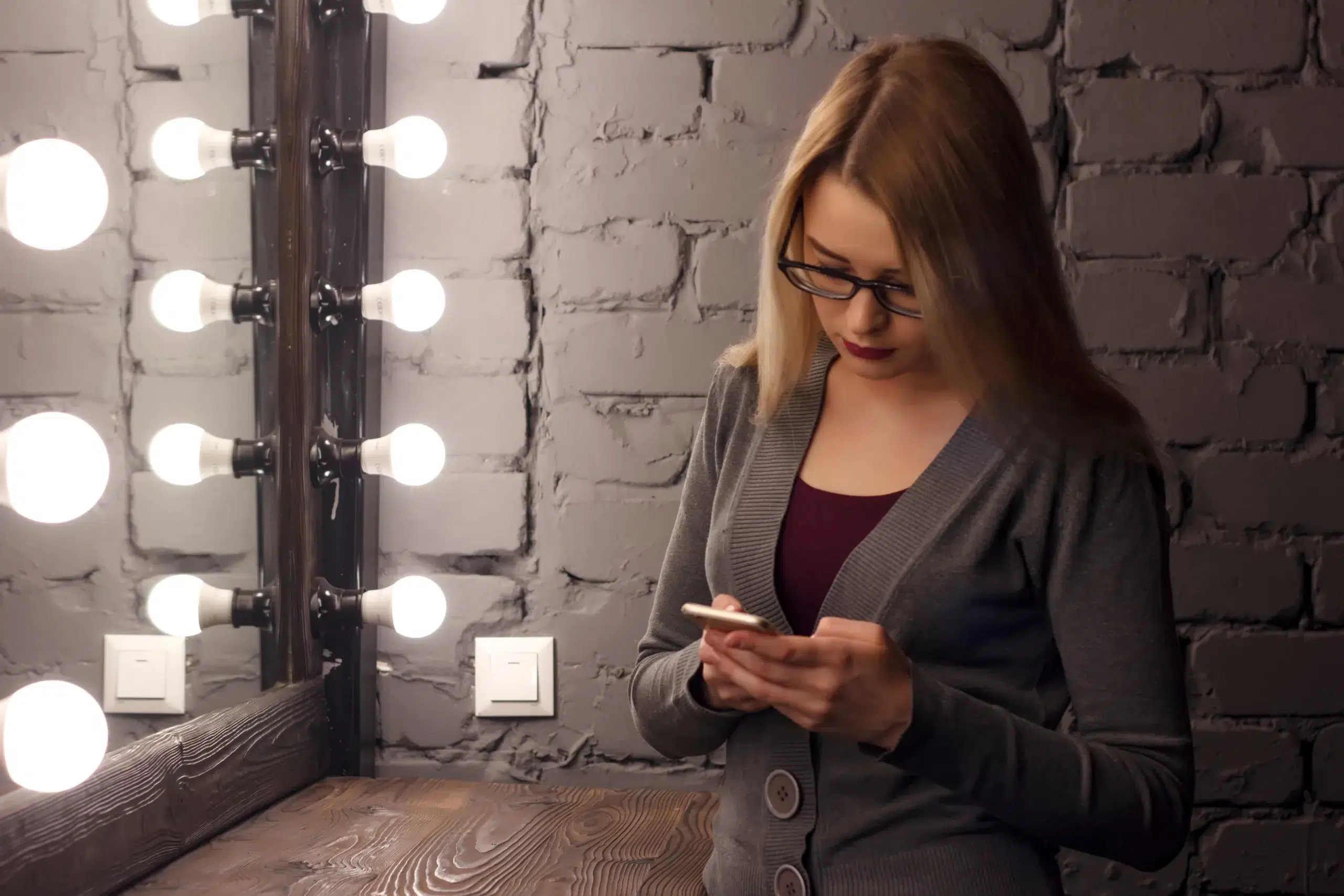 Closeup of sad teenage girl lying in bed using her mobile. Young pretty woman with bored expression looking at message on her cell phone, reading or waiting for call.