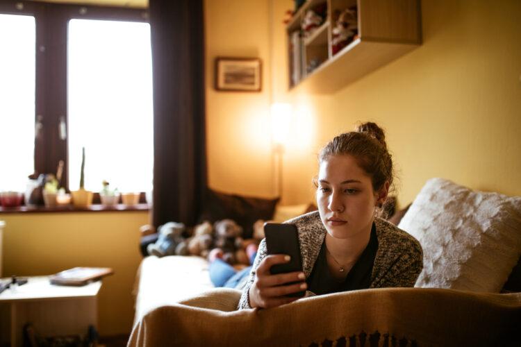 young lady looking worried while staring at the cell phone in her hand