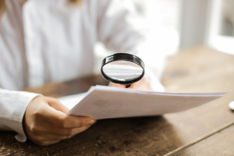 magnifying glass over document, investigating a document.