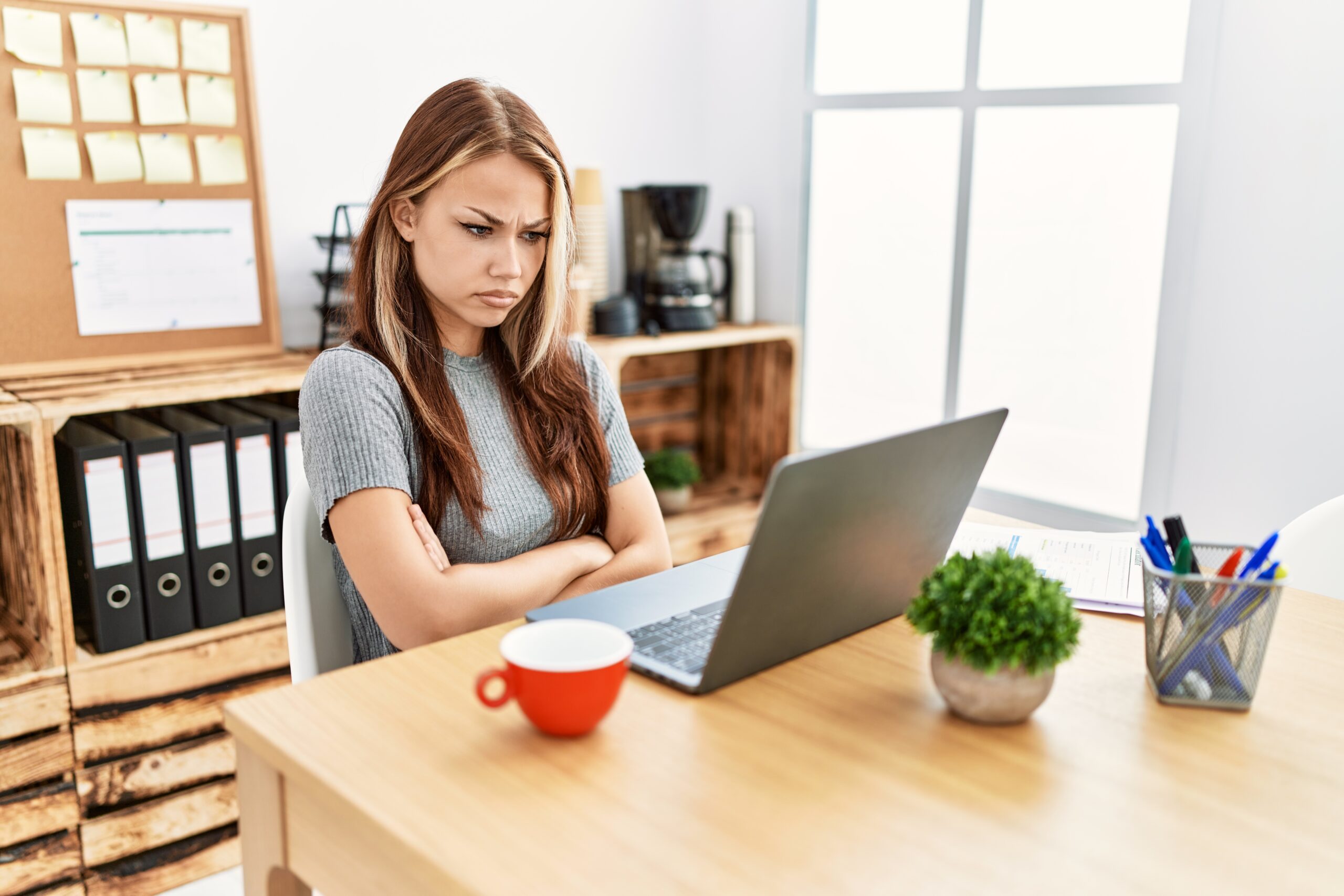 Young brunette woman watching a show on her laptop and with a disapproving expression on face with crossed arms