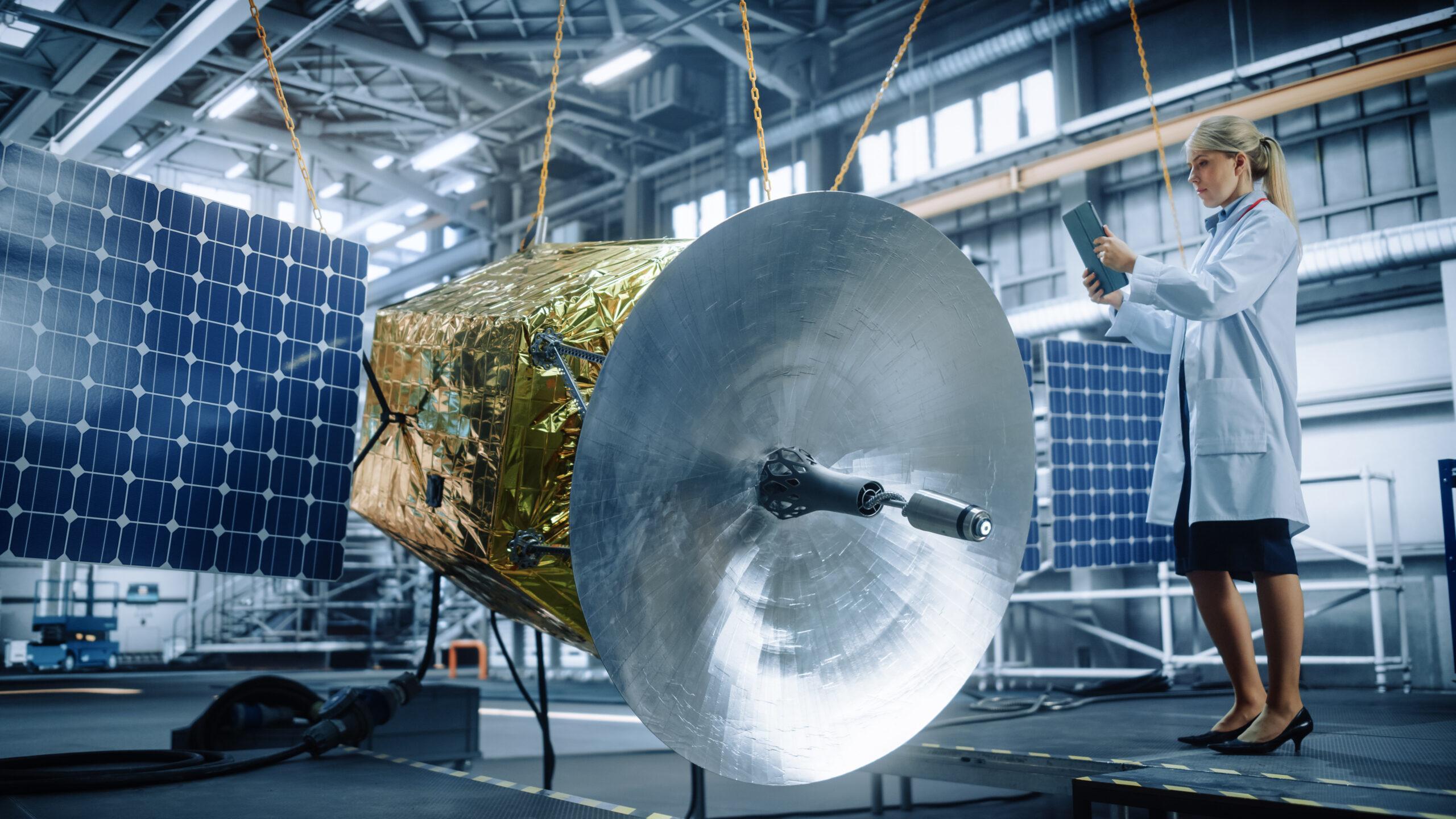 Female engineer using digital tablet computer while working on satellite construction