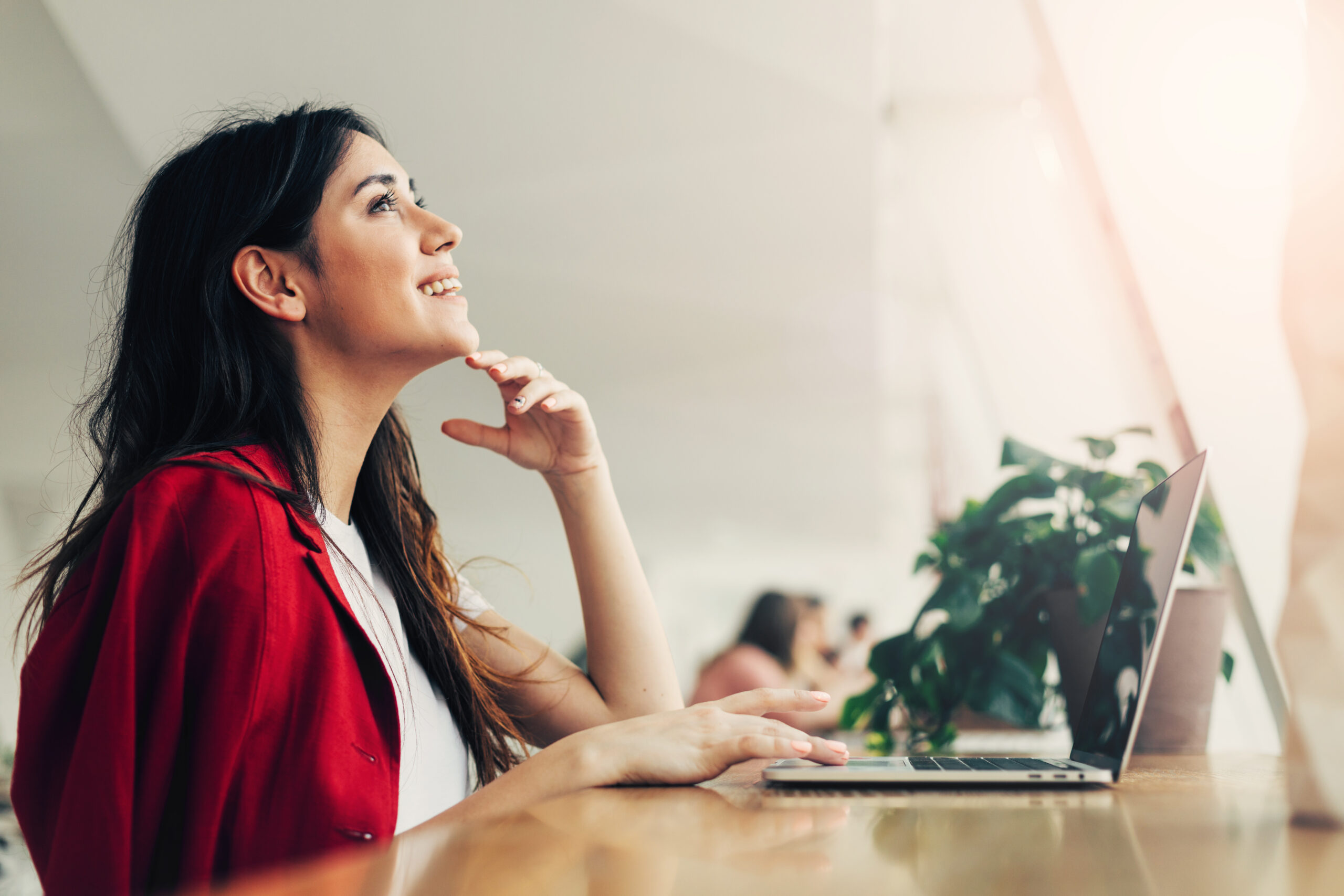 Positive thoughtful nice young woman in coworking. Look up and smile. Daylight. Remote work at table. Alone in room. Buisnesswoman work hard. Take break.