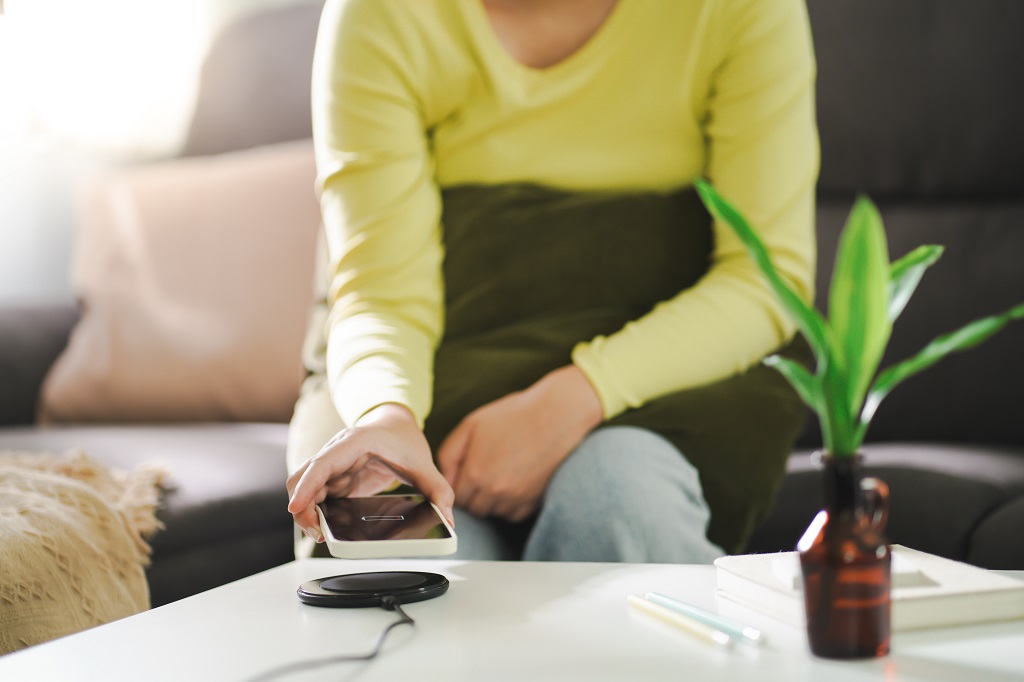 Woman charging mobile phone battery with wireless charging device.