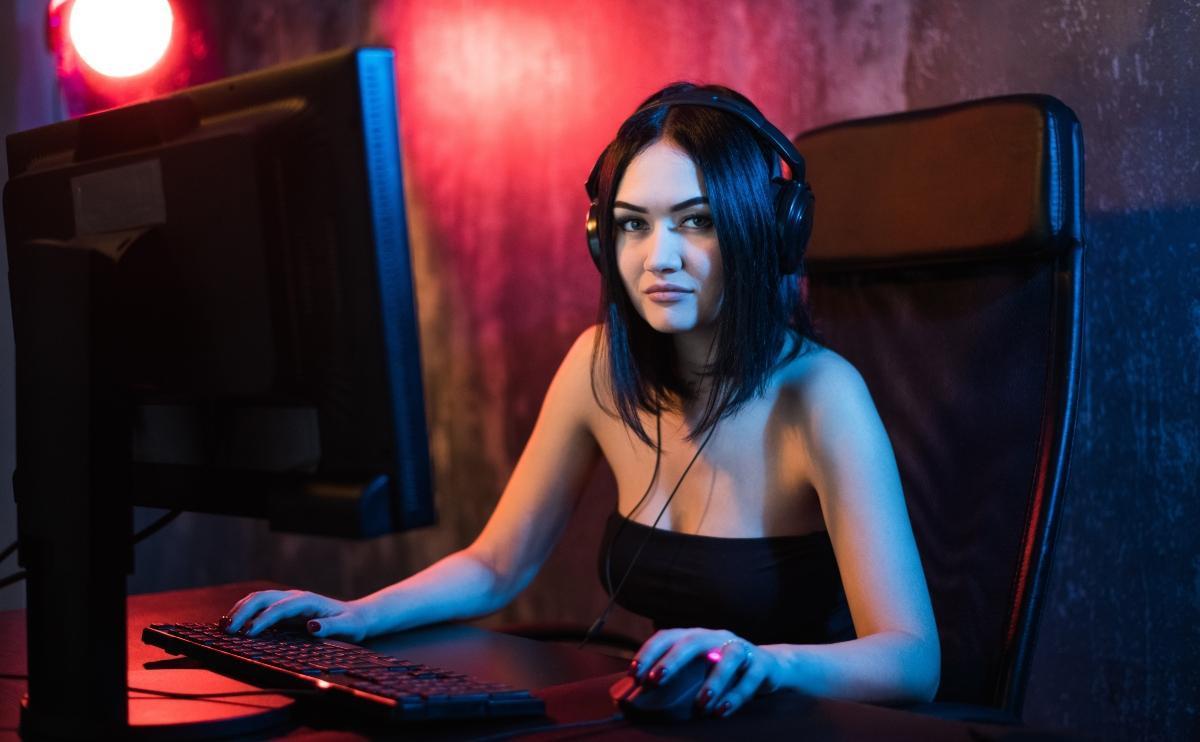 Stunning female with headphones sitting behind a gaming PC  and livestreaming her game