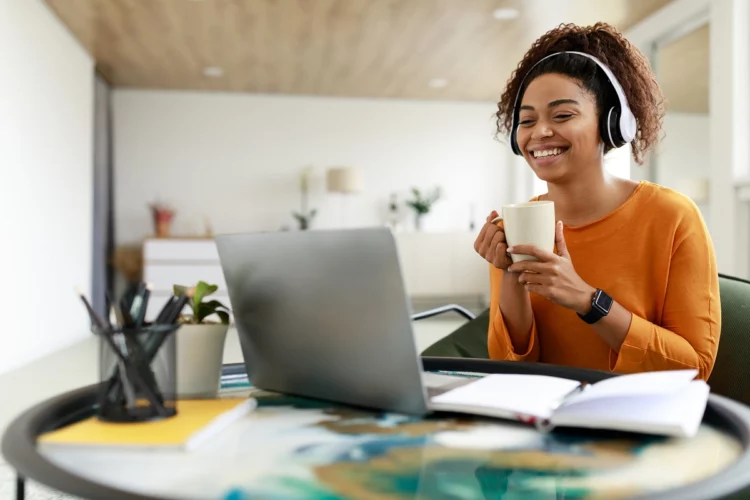 Smiling black woman watching video on computer, drinking coffee
