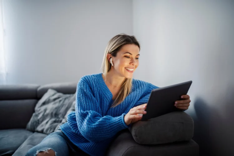 A happy woman watching and enjoying videos on tablet at her cozy home.