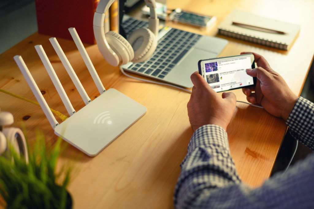  Wireless router and a man using smartphone at desk, laptop in the background