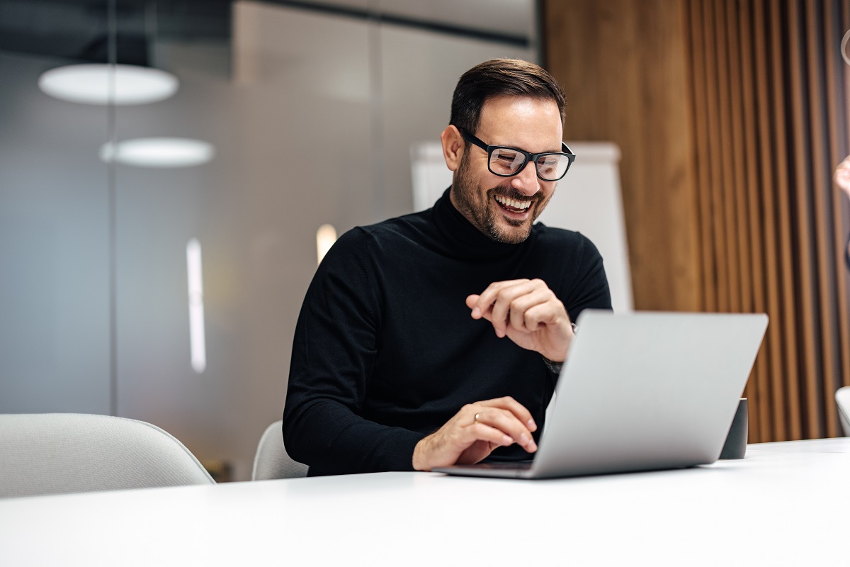 Happy middle-aged man with glasses looking at the laptop screen