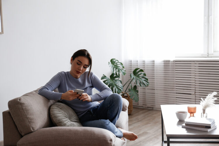 Young brunette woman using phone on sofa with serious look.