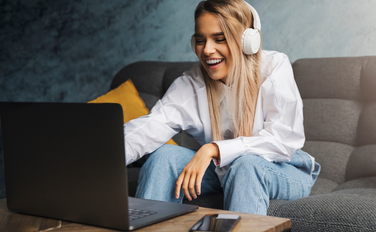Cheerful girl in headphones sitting on sofa in front of laptop