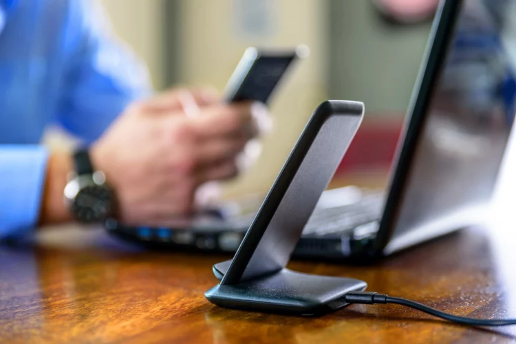 wireless phone charging stand, man holding smartphone at home office in the background.