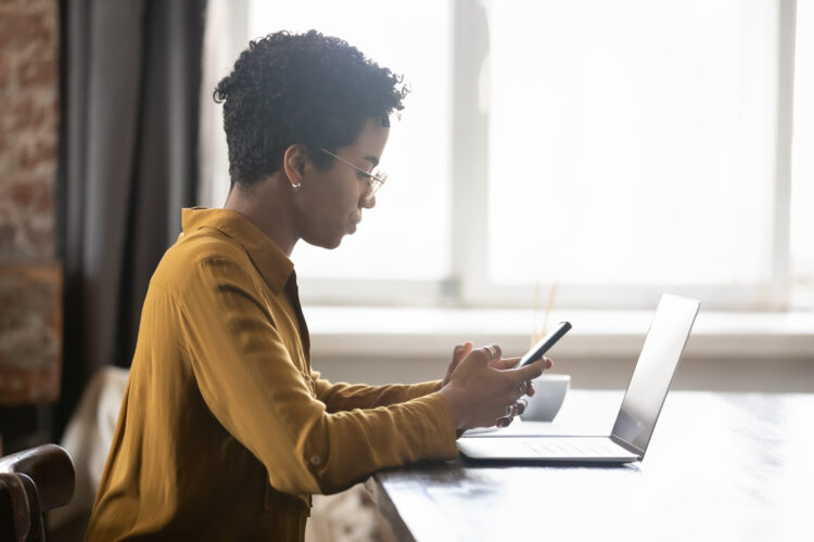 Woman serious face using cellphone in front of laptop at desk