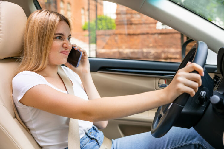 Woman talking on the phone and driving a car, upset because her phone keeps hanging up calls.