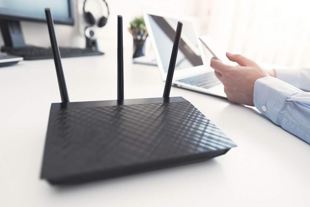 Wireless router on table with man using his smartphone in background.