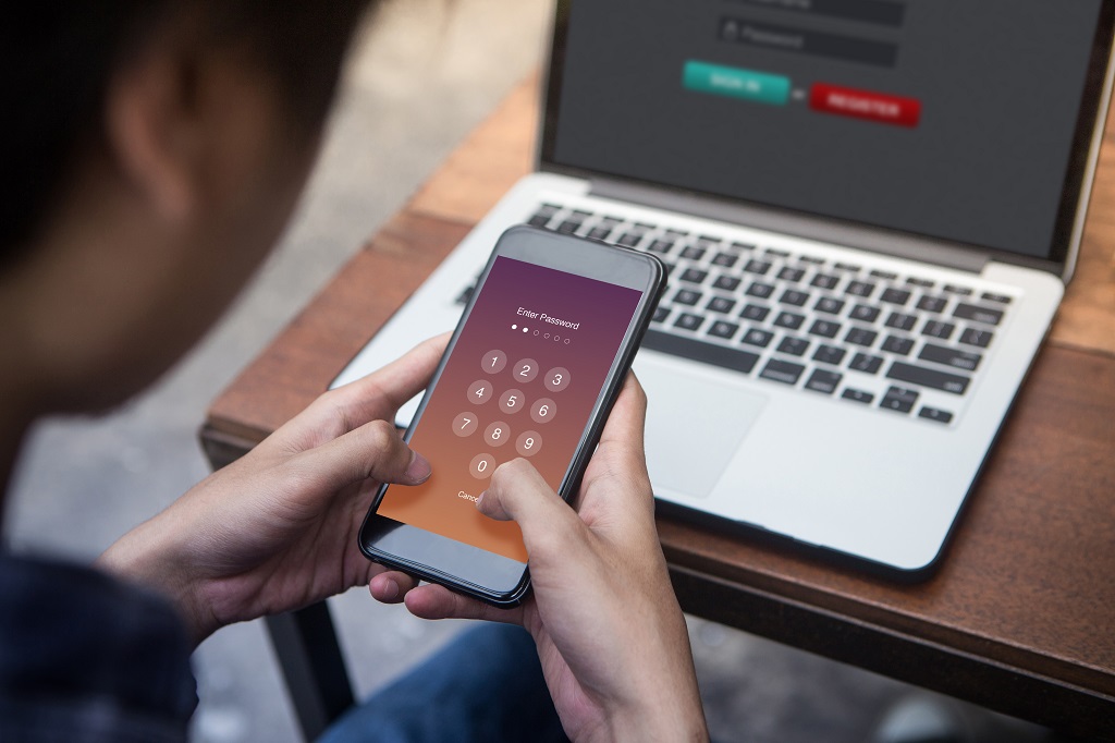 Businessman working on laptop and trying to enter password on his phone.