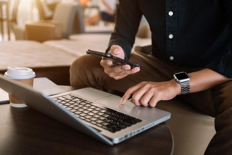 Male hand using smart phone and laptop in a cafe