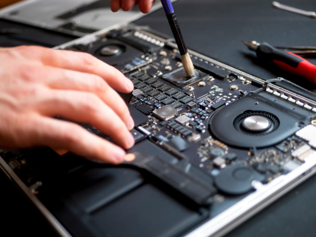 hand with brush clearing the disassembled laptop from dust and dirt.