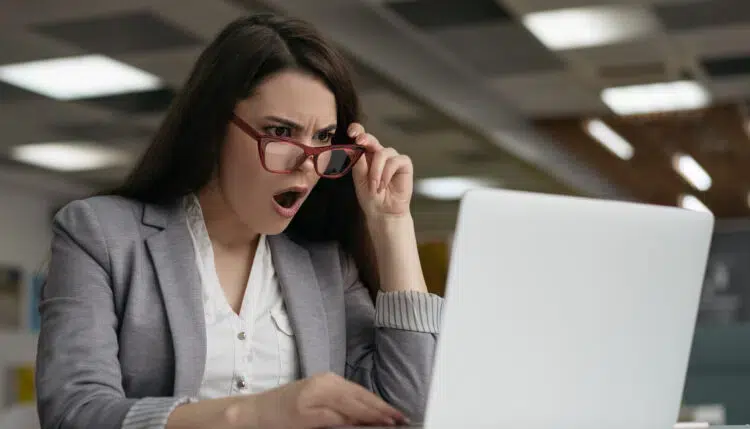 Female office worker looking at laptop shocked after discovering an employee secretly tried to copy files from a work computer to usb drive.
