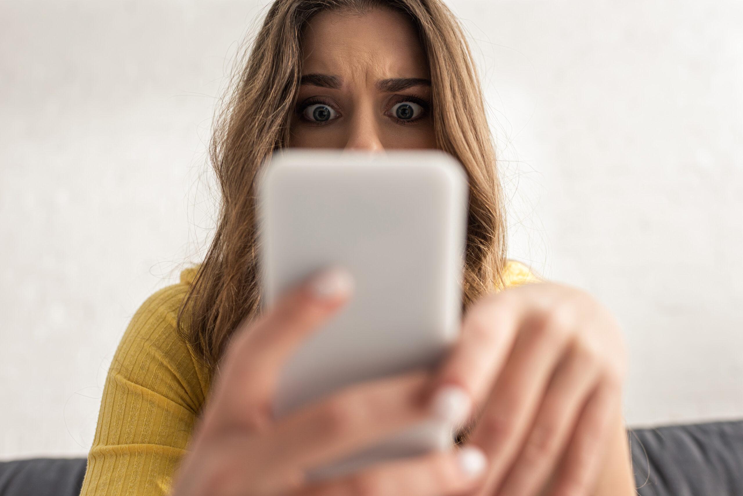Shocked face of a woman half-covered by the smart phone she is using