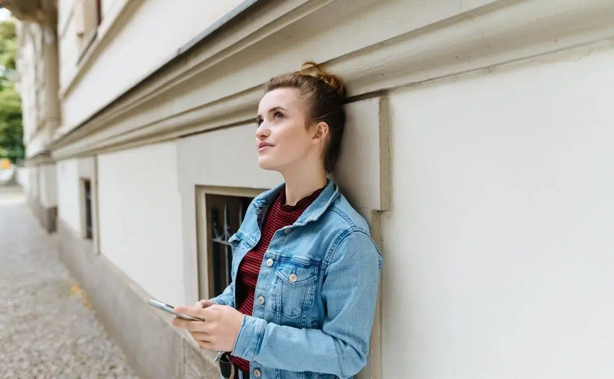 Young woman standing deep in thought wondering if she should cancel her latest sent follow request on Instagram.