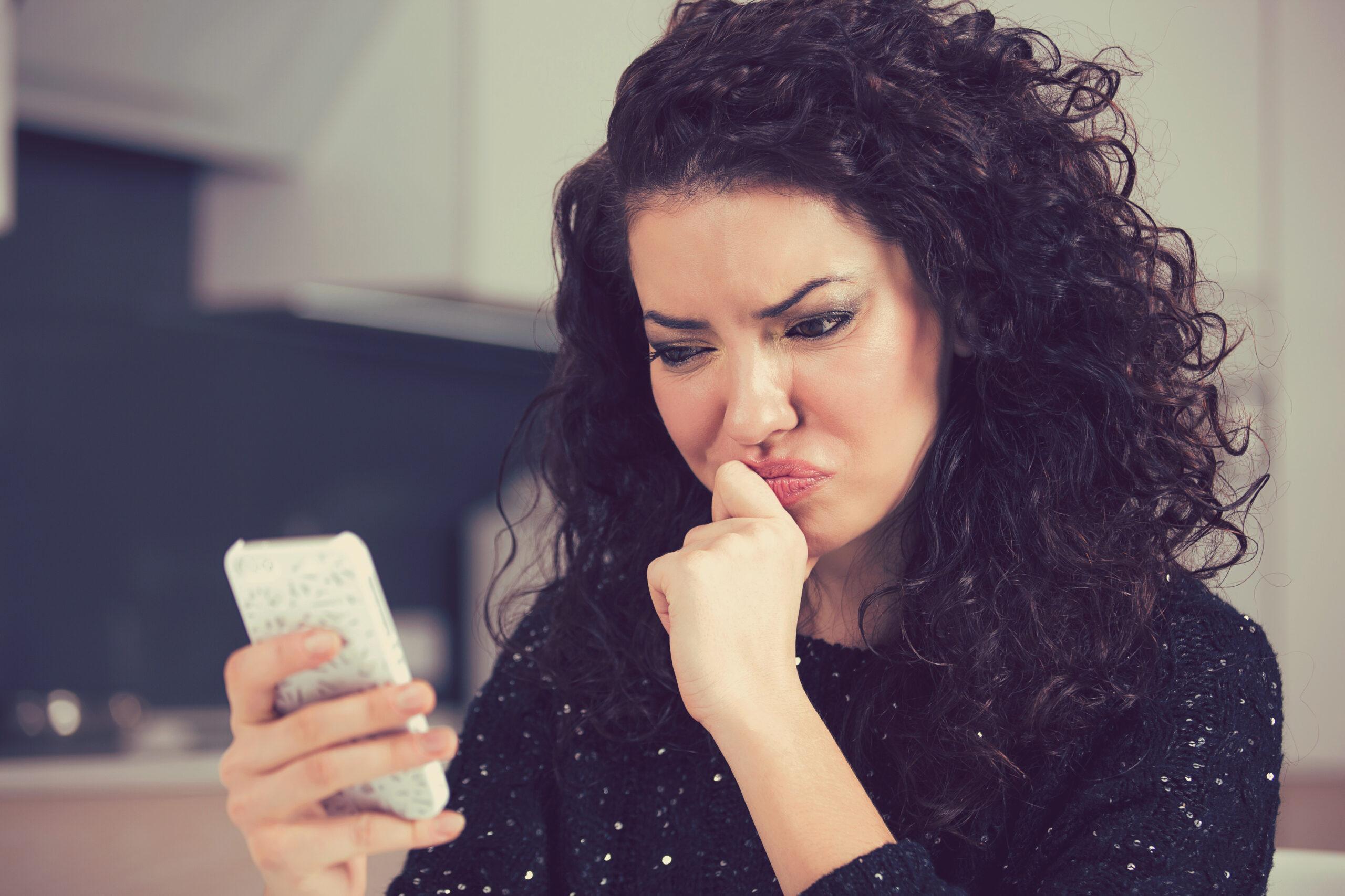 Upset confused young woman suing mobile phone reading text messa