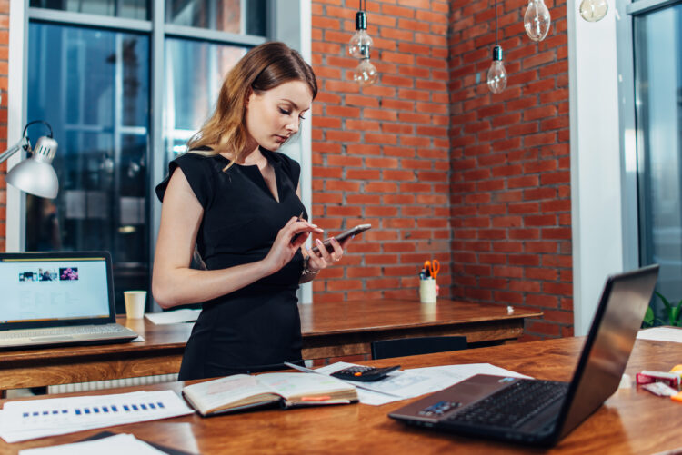 woman working using smartphone standing at her workplace in creative office