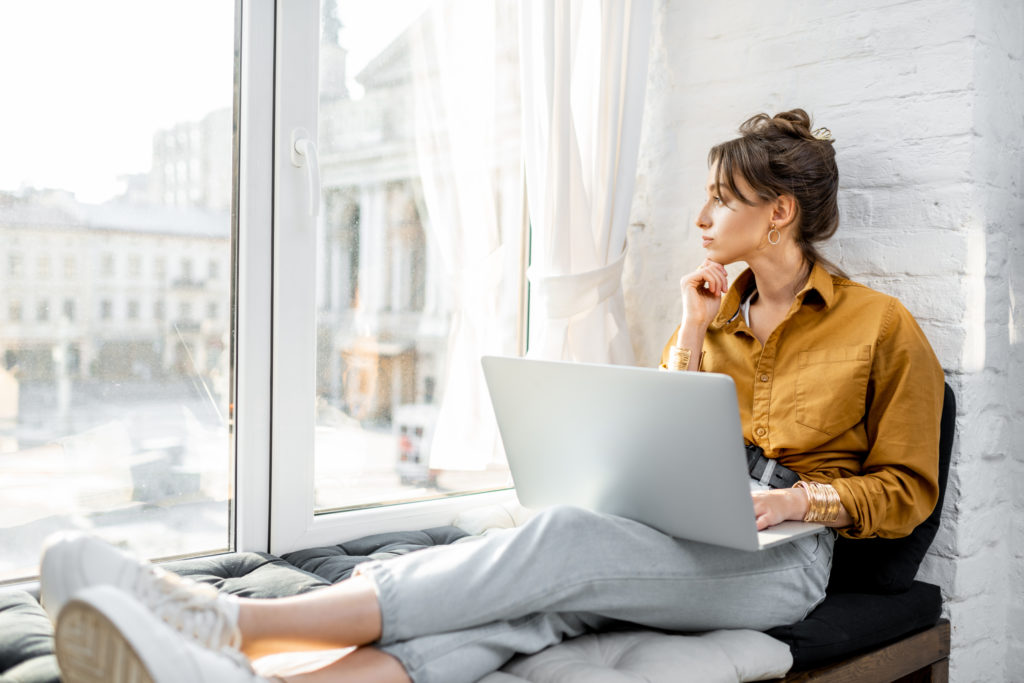 Woman with laptop working at window seat.